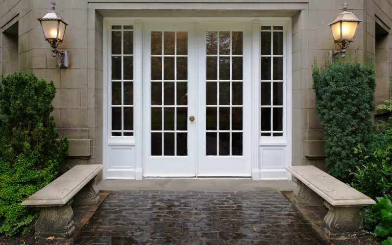 Elegant stone walkway bordered by stone benches leading to a double glass paned front door with two large front lanterns