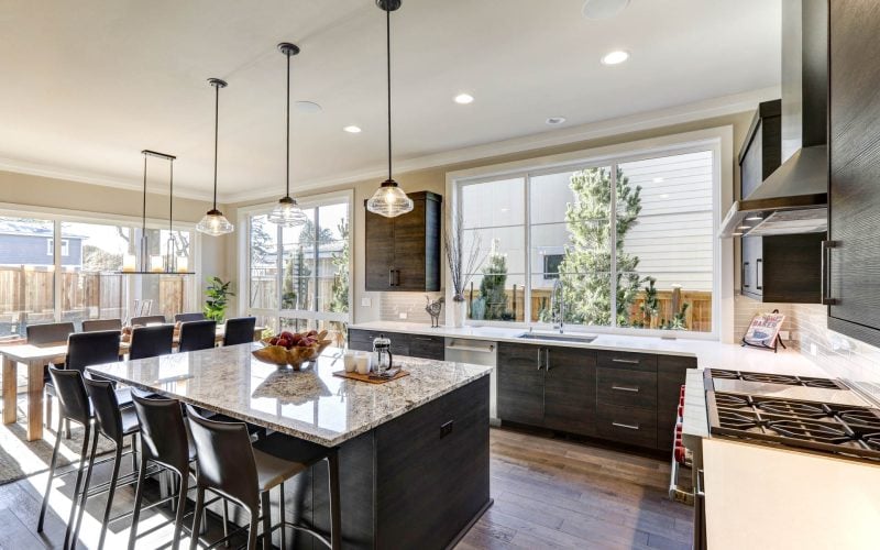 Modern gray kitchen features dark gray flat front cabinets paired with white quartz countertops and a glossy gray linear tile backsplash. Bar style kitchen island with granite counter. Northwest USA